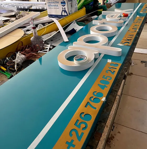 A teal shop fascia on the workbench with white raised letters being fixed to it.