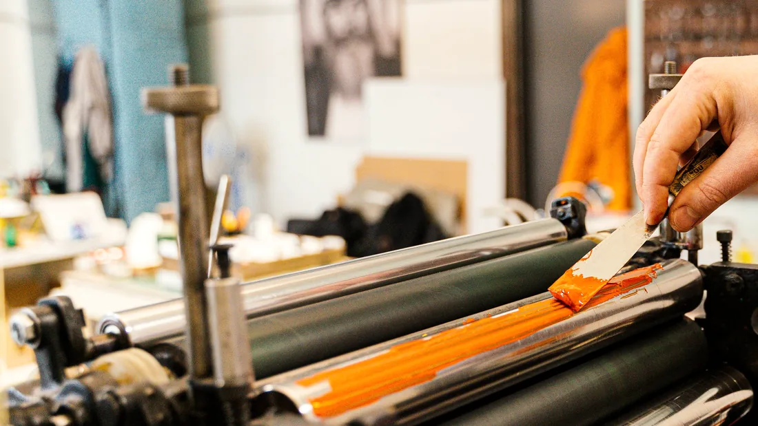 Orange ink being worked onto the rollers of a printing press.