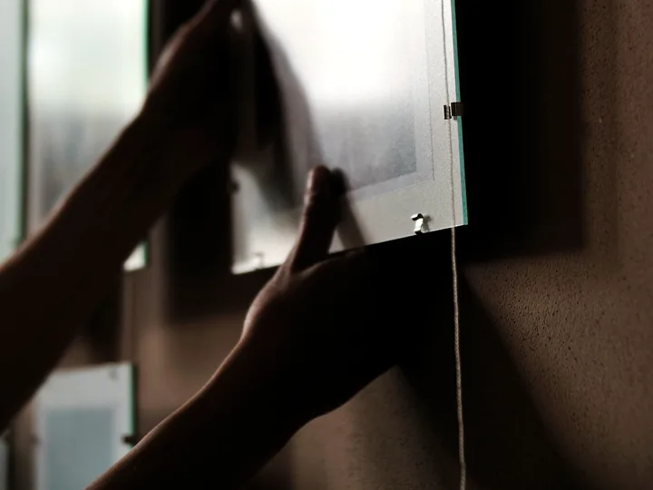 Hands mounting a frosted panel onto a dark wall.