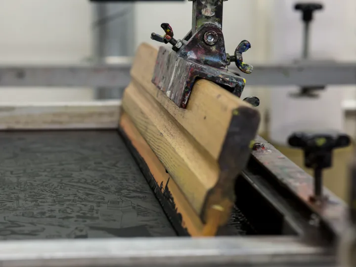 A squeegee resting on a screen-printing frame.