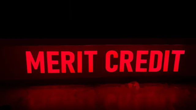 Red illuminated letters spelling MERIT CREDIT above a glossy floor.