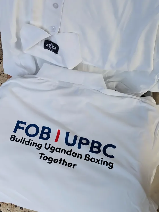 A white polo shirt printed with FOB UPBC Building Ugandan Boxing Together.