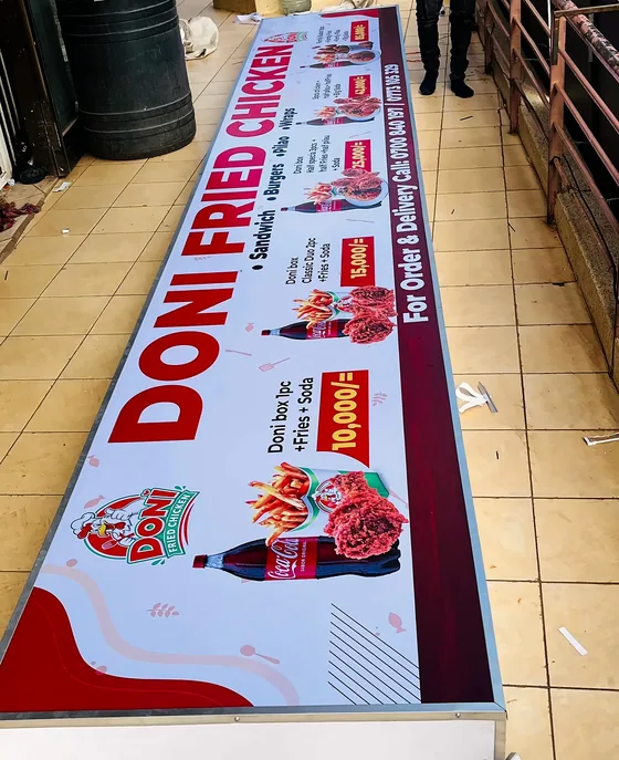 A long printed banner for a fried chicken restaurant laid out on a tiled floor.