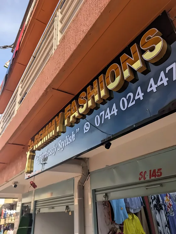 Gold dimensional lettering on a dark shop fascia with a phone number, seen from below.