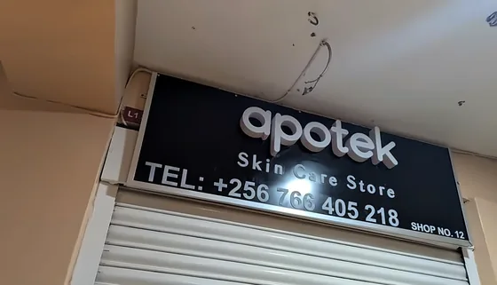 Black apotek skin care store fascia with white lettering, lit above a closed shutter.