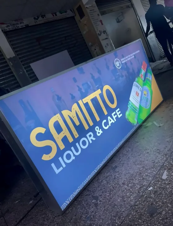 Blue lightbox sign with yellow Samitto Liquor and Cafe lettering, propped on a pavement.