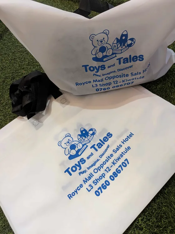 White non-woven tote bags printed in blue with the Toys and Tales logo.