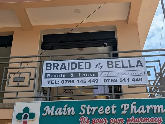 Two fascia boards on a building front: Braided by Bella above Main Street Pharmacy.